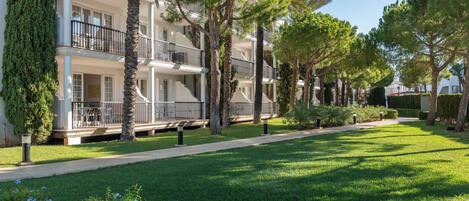 A multi-story hotel with balconies, surrounded by well-maintained lawns and trees.