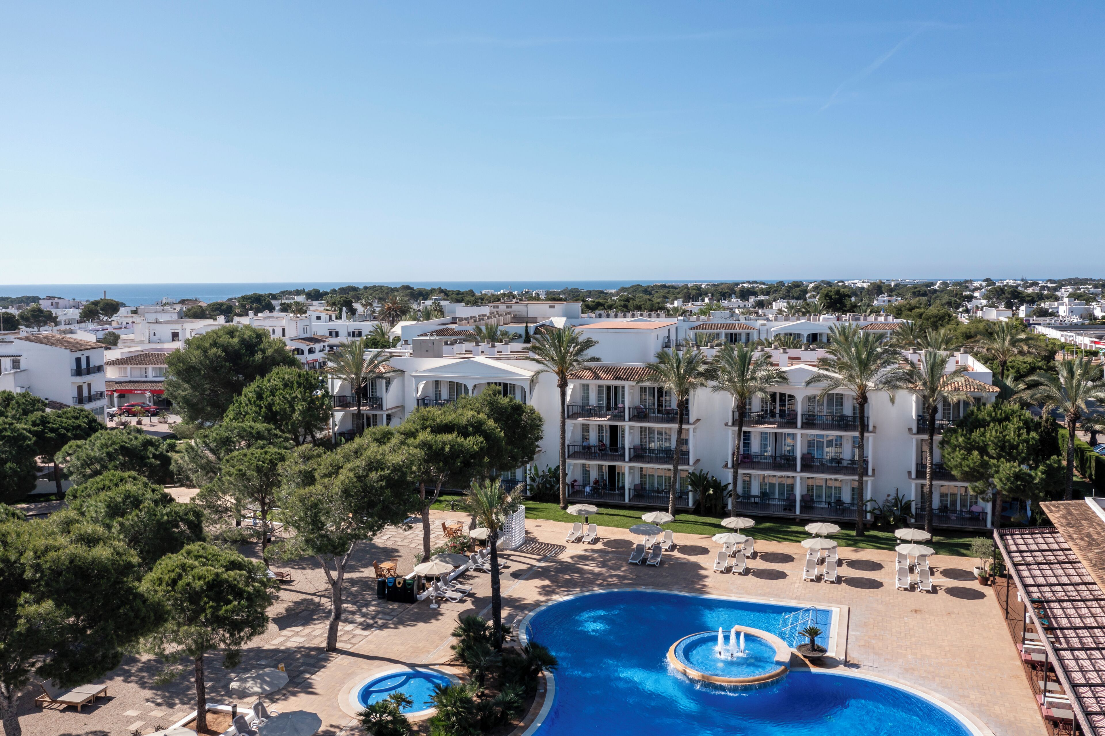 A resort with a large swimming pool, palm trees, and a view of the sea.