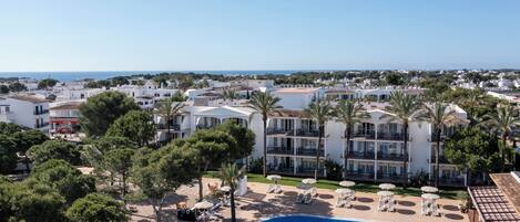 A resort with a large swimming pool, palm trees, and a view of the sea.