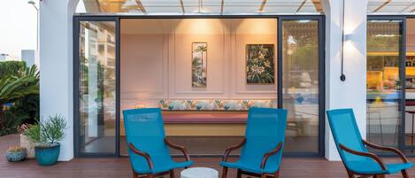 A modern outdoor seating area with two rocking chairs and a round table, overlooking a building with large glass doors and a bench inside.