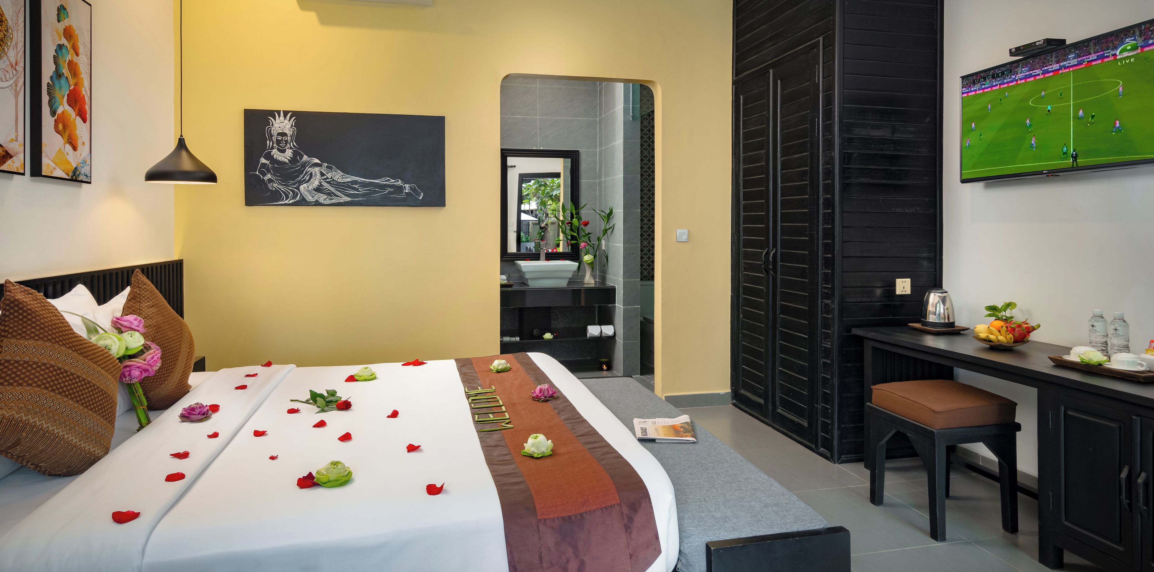 A hotel room with a bed, a desk, a TV, and a bathroom visible through an open door.