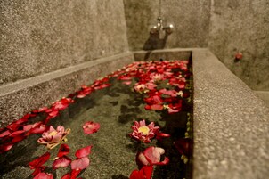 Un estanque con bordes de piedra, pétalos de rosa y flores.