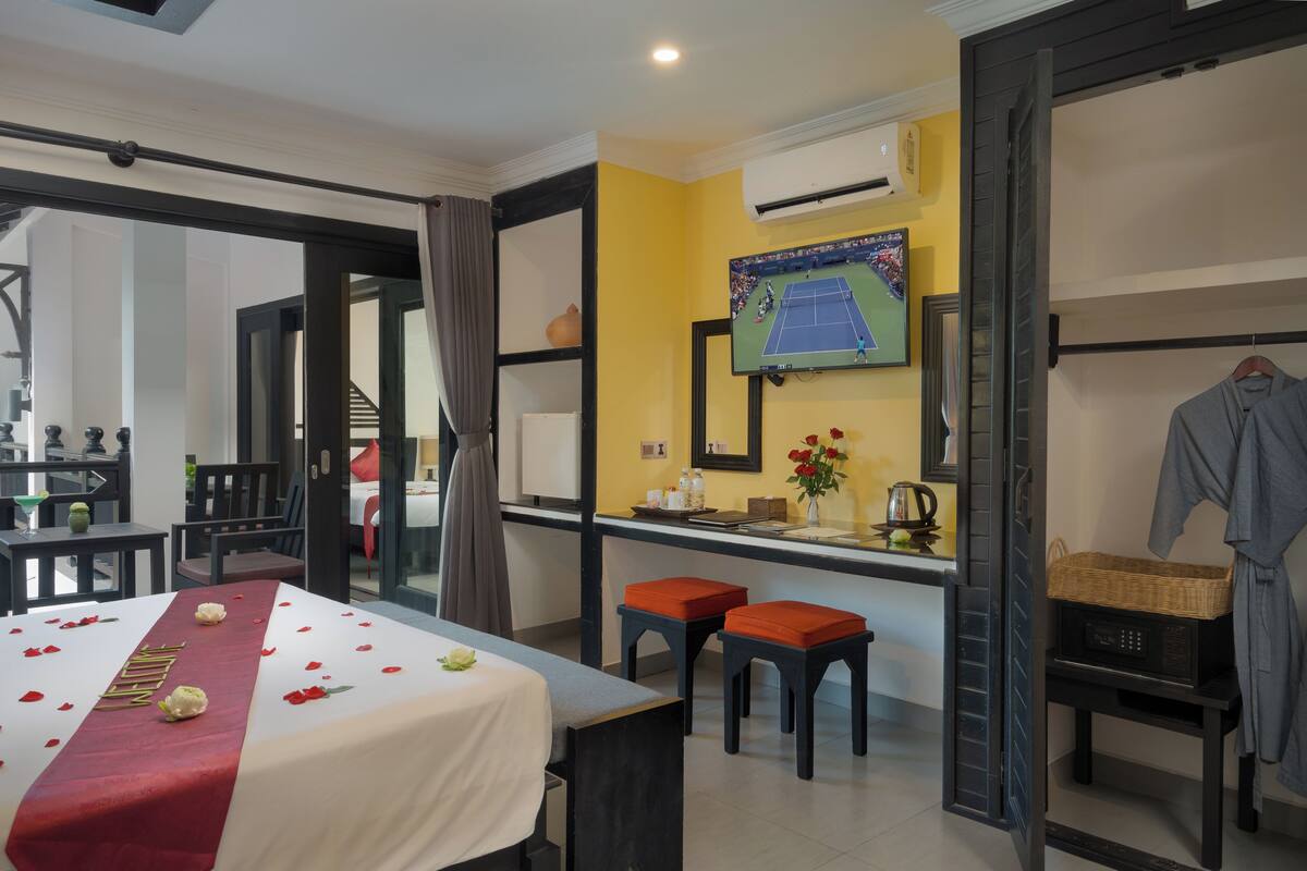 A hotel room with a bed, two chairs, a small table, a TV, and a window.
