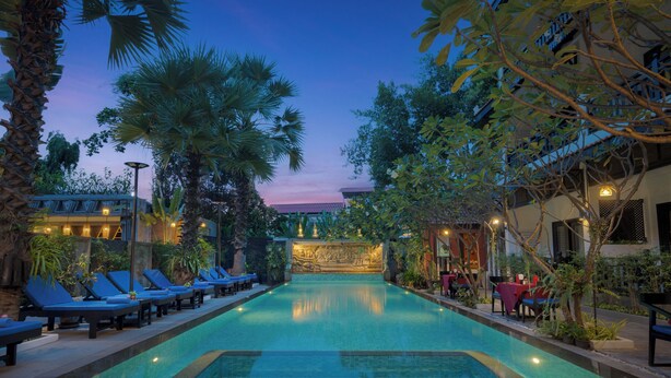 A pool area with lounge chairs, a decorative wall, and surrounding vegetation. - Khmer Mansion Boutique Hotel (Siem Reap)
