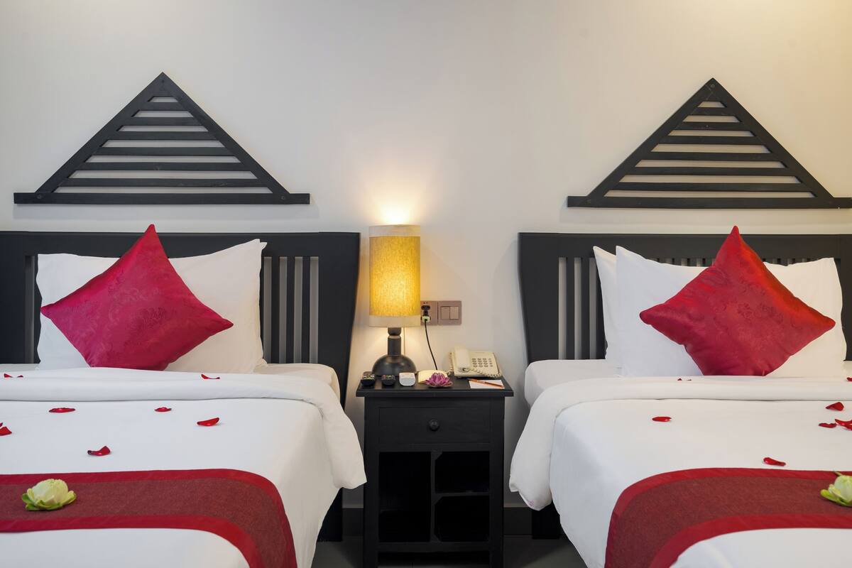 A hotel room with two beds, each with red and white bedding, a bedside table with a lamp, and a phone.