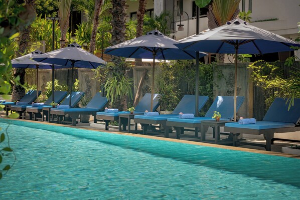 A poolside area with lounge chairs and umbrellas, surrounded by greenery.