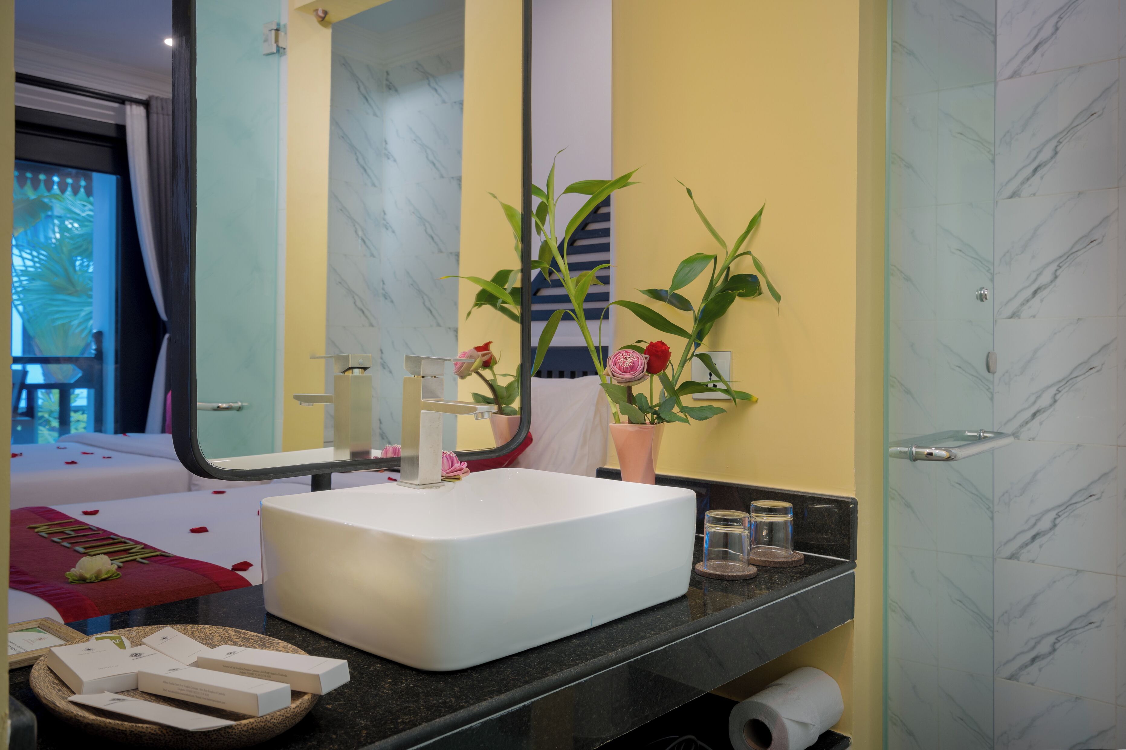 A bathroom with a white sink, a large mirror, a potted plant, and a shower area with marble tiles.