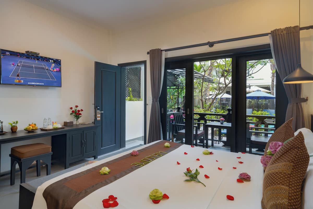 A hotel room with a bed, a desk, and a TV displaying a tennis match.