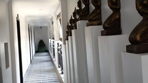 A hallway with a tiled floor, white walls, and a row of golden statues on pedestals. - Khmer Mansion Boutique Hotel (Siem Reap)