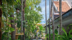 A narrow pathway flanked by lush tropical plants and traditional architecture, leading to a building with a tiled roof. - Khmer Mansion Boutique Hotel (Siem Reap)