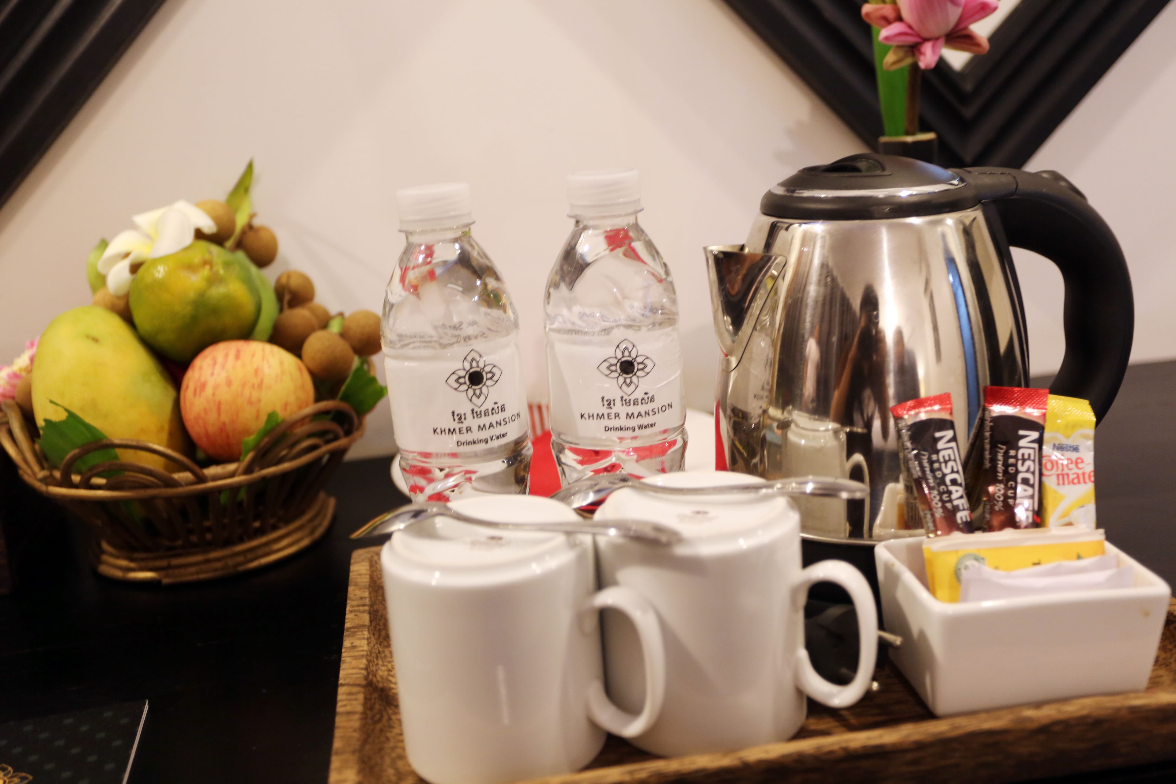 A breakfast tray with fruits, bottled water, coffee mugs, a coffee pot, and Nescafé instant coffee packets.