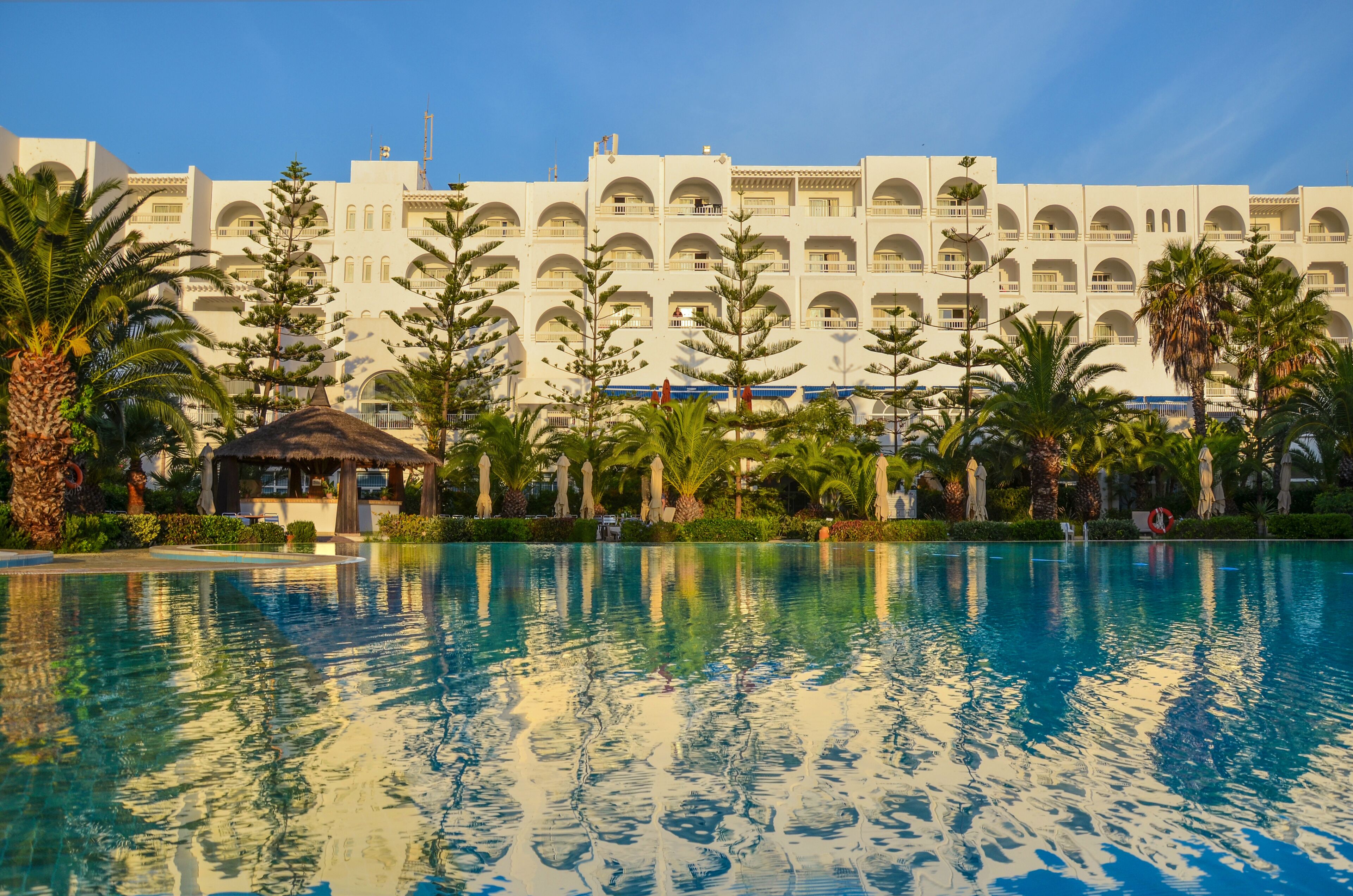A hotel with a large pool, palm trees, and a building with multiple balconies.