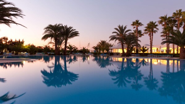 A serene pool area with palm trees and lounge chairs, reflecting the sunset.