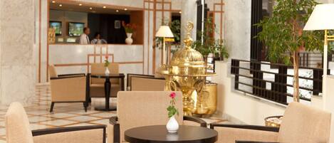 A lobby with a reception desk, seating area, and decorative elements like a golden lamp and a vase with a flower.