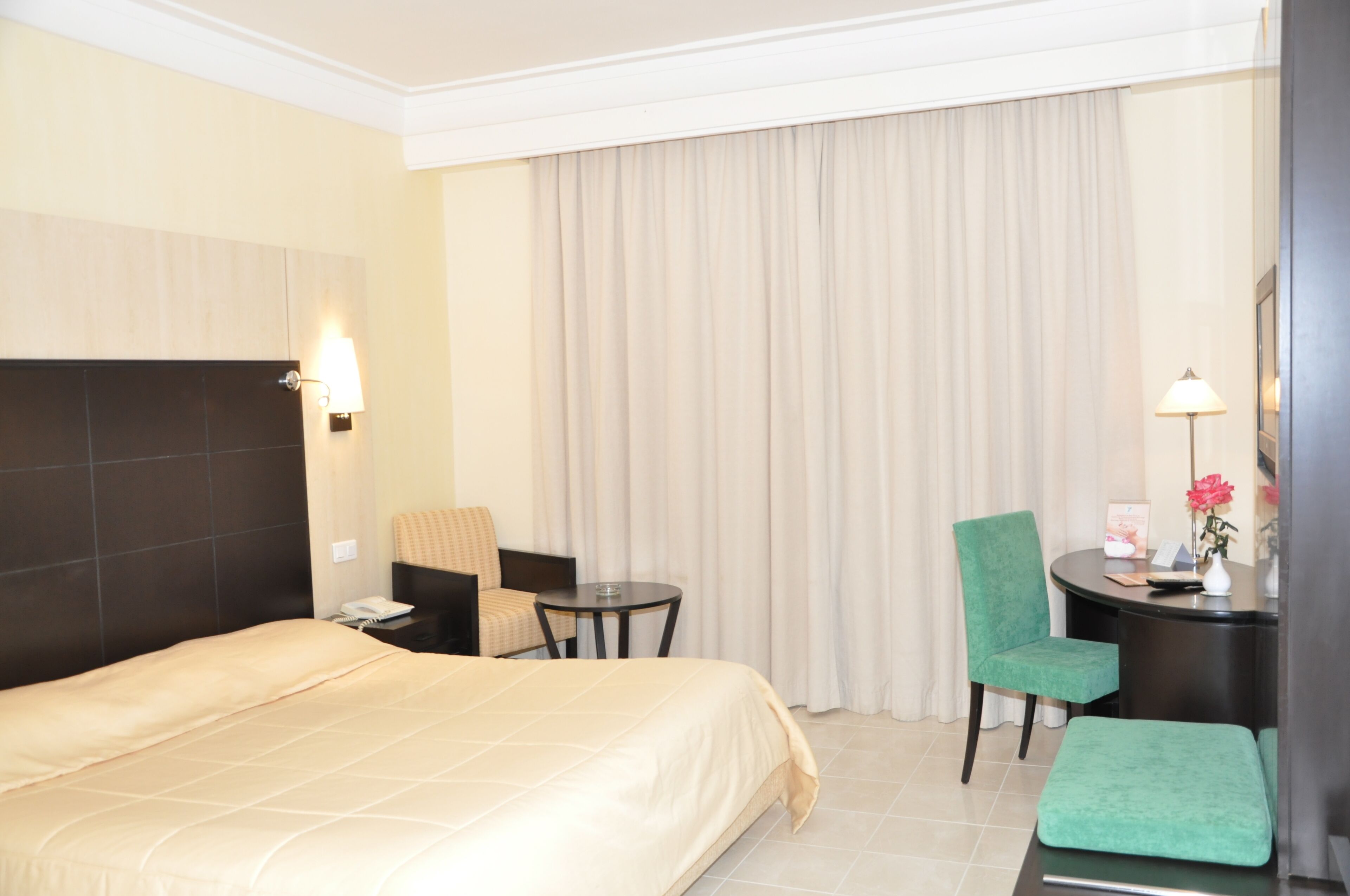 A hotel room with a large bed, a desk with a chair, a small table, and a green ottoman.
