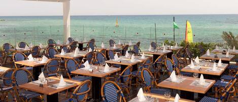 An outdoor dining area with tables and chairs, overlooking the sea.