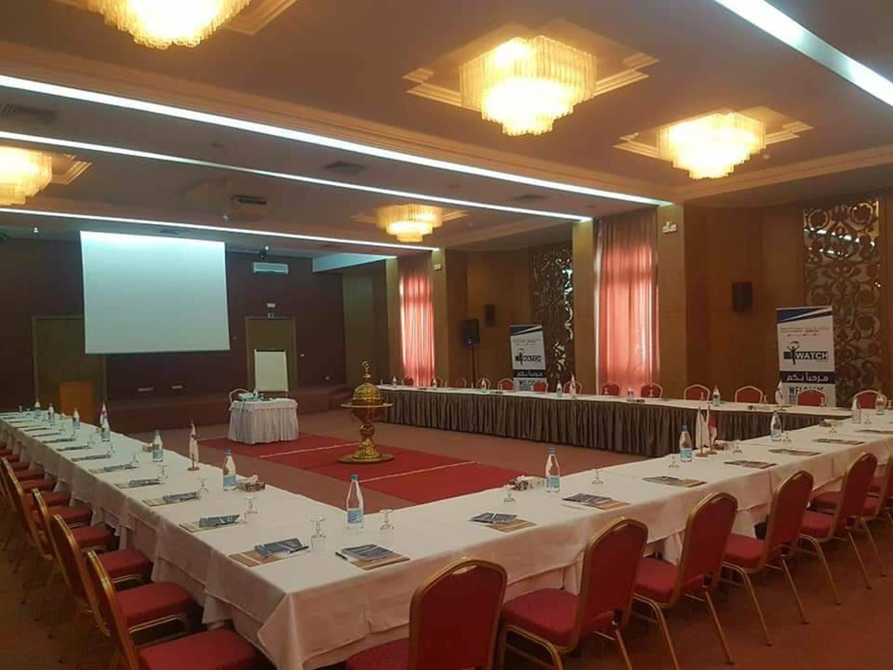 A conference room with a long table, red chairs, and a stage with a podium.