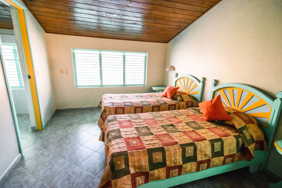 Una habitación con dos camas, techo de madera, una ventana y una puerta.