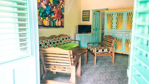 A room with a wooden sofa, two wooden chairs, a small table, a television, and colorful cabinets. - Las Palmas Residence (Las Terrenas)