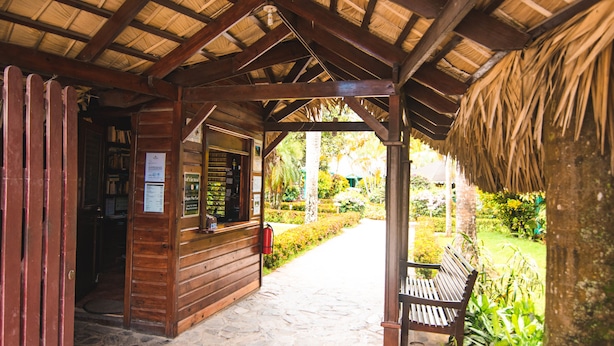 A wooden structure with a thatched roof, a bench, and a pathway leading to a garden area. - Las Palmas Residence (Las Terrenas)