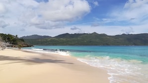 A beach with clear turquoise water, sandy shore, and green hills in the background. - Las Palmas Residence (Las Terrenas)