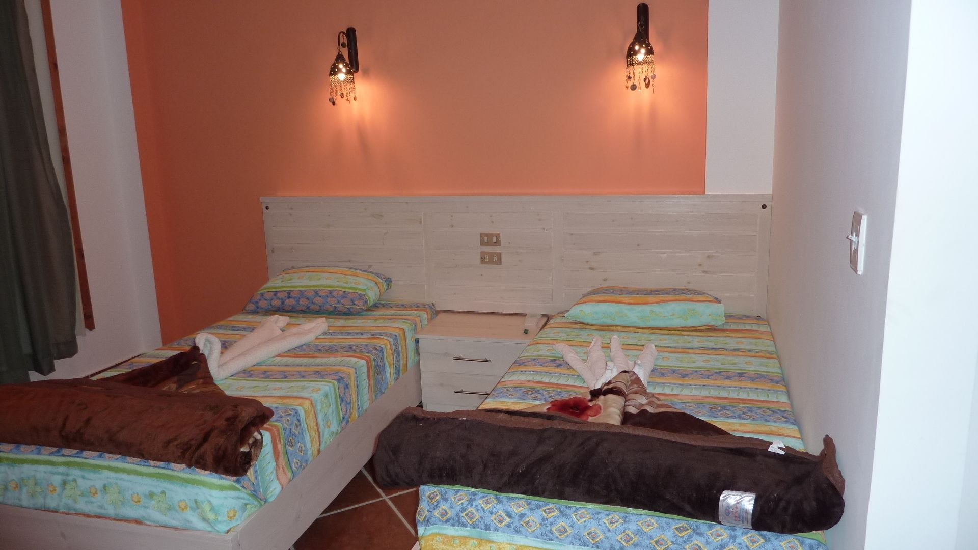 A hotel room with two beds, each with a patterned bedspread and pillows. There are wall-mounted lights above the beds.