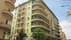 Un edificio residencial de varios pisos con balcones, fachada verde y cielo despejado.