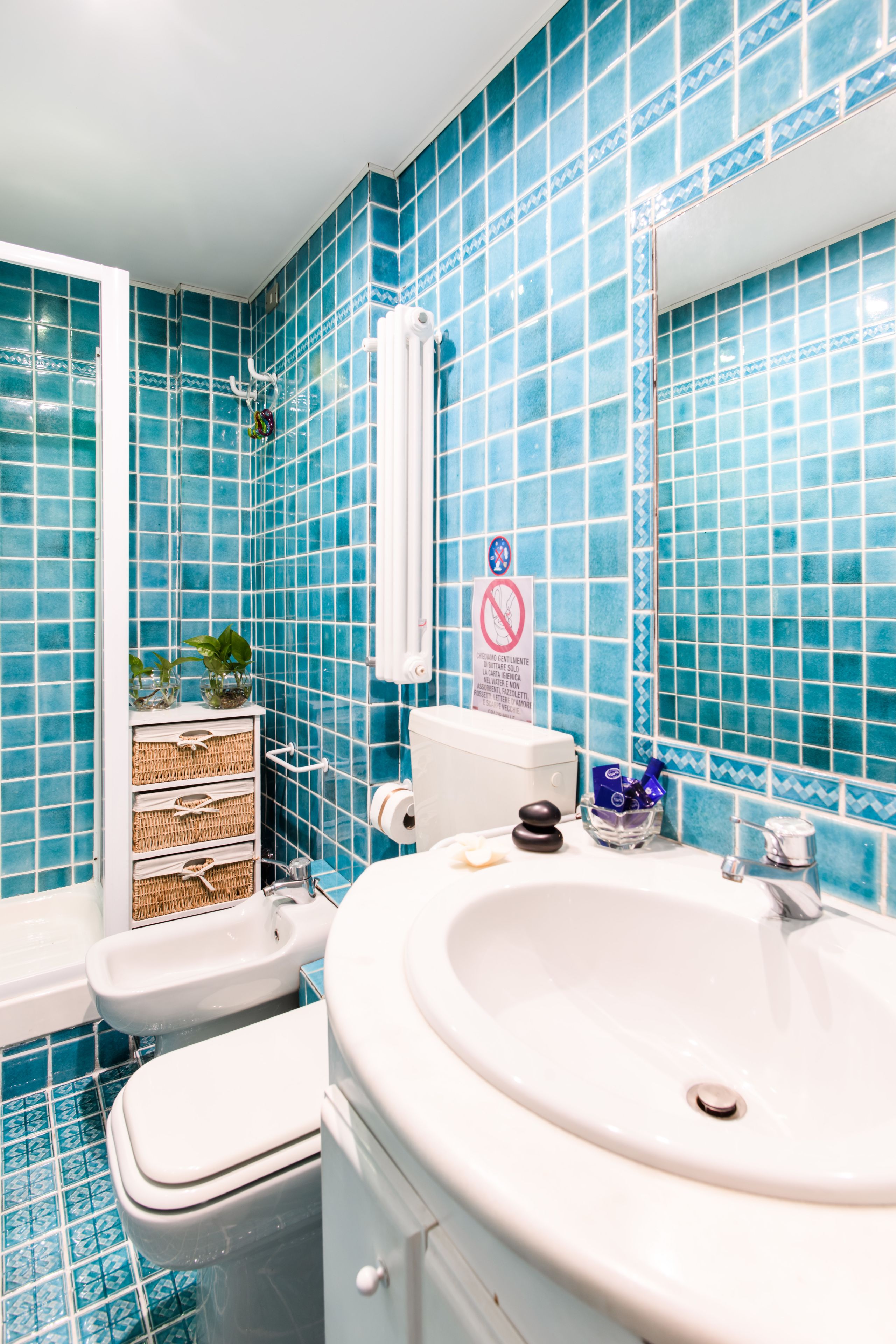 A bathroom with blue tiles, a sink, a toilet, a bidet, and a towel rack.