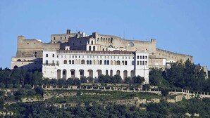 Un edificio grande e histórico con múltiples arcos y una estructura fortificada en una colina.