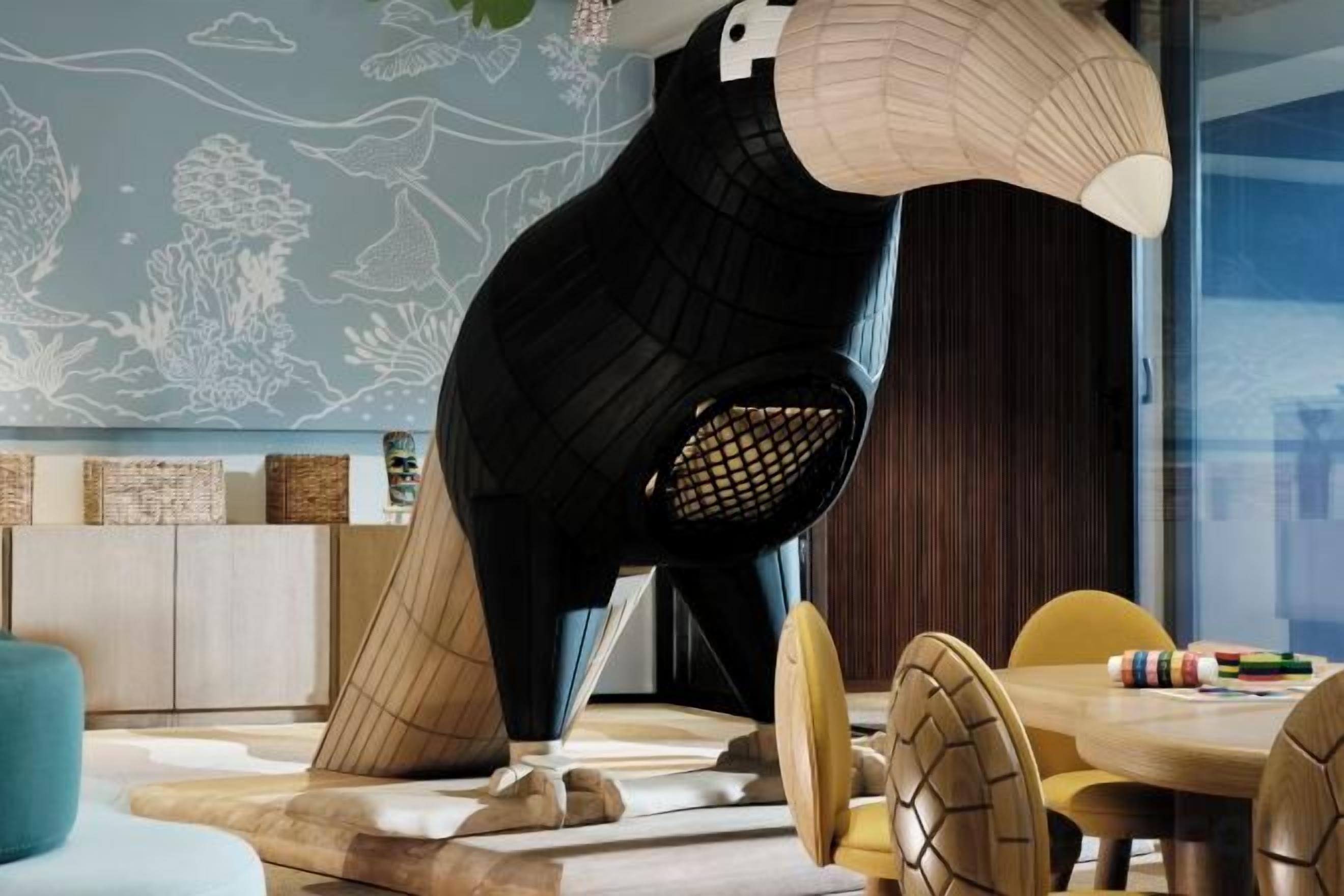 Un intérieur moderne agrémenté d’une sculpture originale, un coin repas avec des chaises en bois et un mur orné d’une fresque sur le thème de la nature.