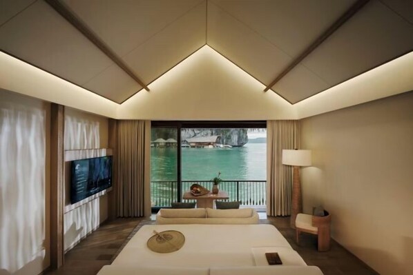 Une chambre d’hôtel moderne dotée d’un grand lit, d’un téléviseur à écran plat, d’un balcon avec vue sur l’eau et d’une petite table avec une lampe.