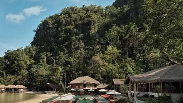 Un resort con edificios de techo de paja, una zona de piscina y vistas a una ladera boscosa.