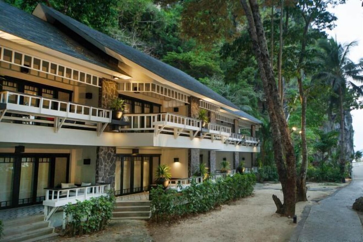 Un hôtel de deux étages doté d’un balcon à chaque niveau, entouré d’une végétation luxuriante.