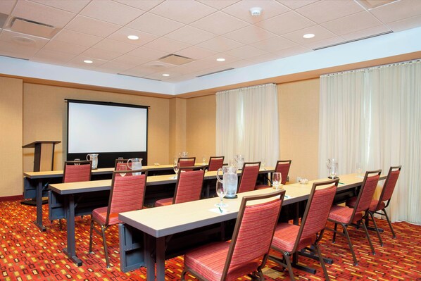 A conference room with a large screen, multiple tables, and chairs. - Courtyard Peoria Downtown (Peoria)