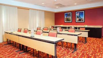 Une salle de conférence dotée de plusieurs tables, de chaises et d’un mur d’accent rouge orné de deux tableaux encadrés.