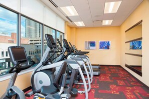 Un gimnasio con cintas de correr alineadas contra una pared con ventanas, suelo alfombrado y equipo de ejercicio.