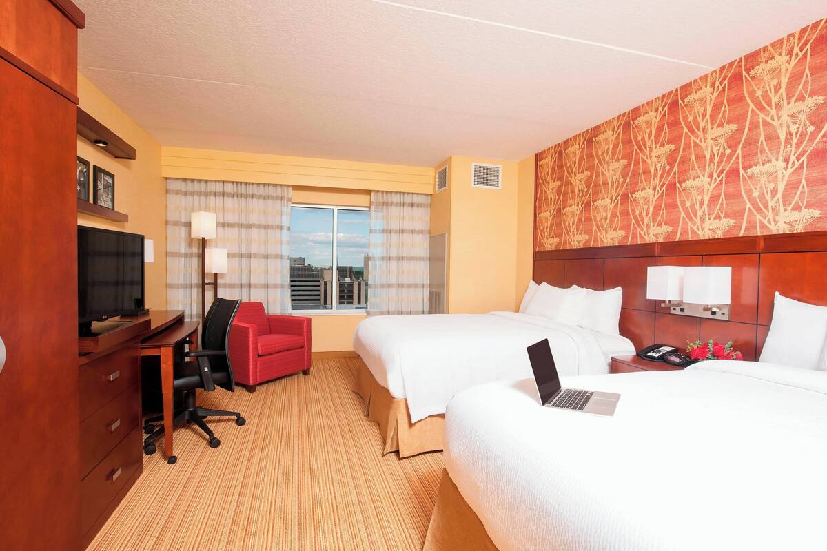 Habitación de hotel con dos camas, un escritorio con silla, televisión y ventana con cortinas.