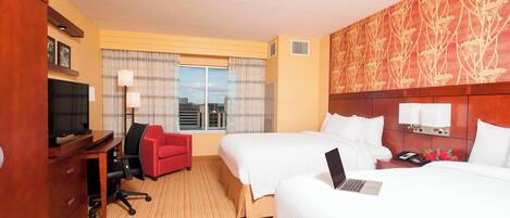 A hotel room with two beds, a desk with a chair, a TV, and a window with curtains.