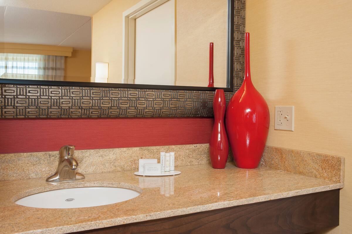 Un baño con un lavamanos, dos jarrones rojos, un espejo y una pared con diseño.