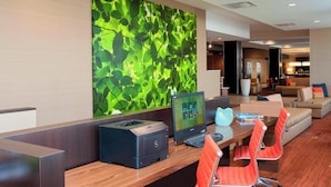 Un moderno vestíbulo de hotel con un mostrador de recepción, un amplio muro abstracto verde, un área de descanso con sillas anaranjadas y una computadora.