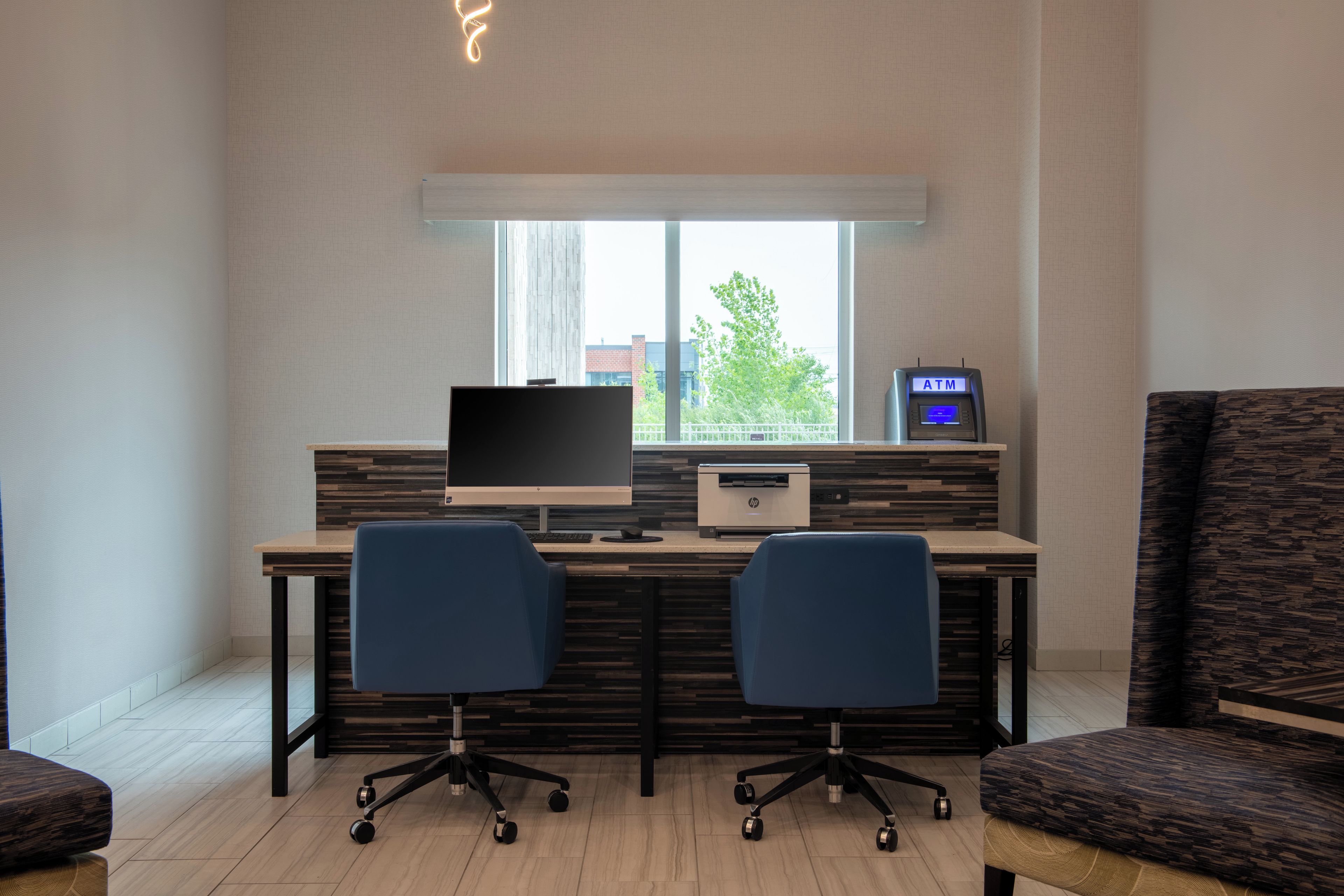 A modern office space with a desk, two chairs, a computer, an HP printer, and an ATM.