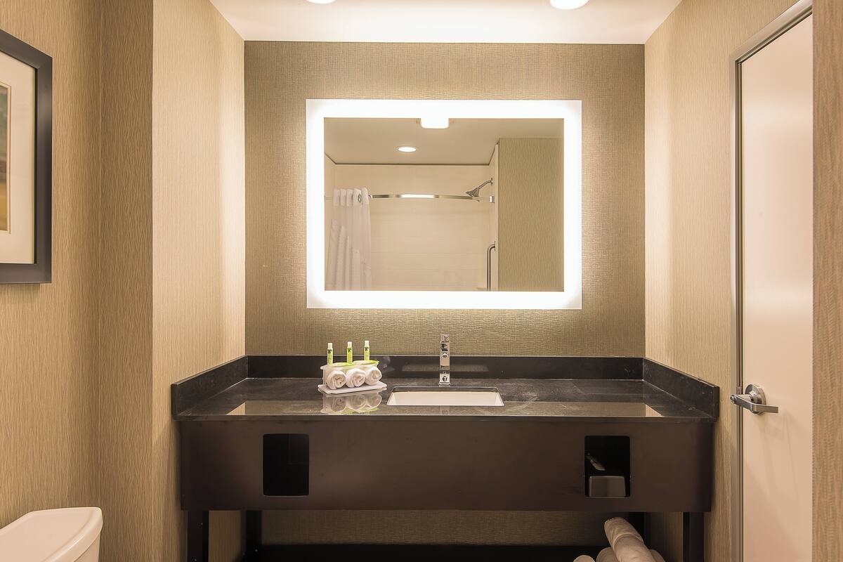 A modern bathroom with a large mirror, a sink, and a toilet.
