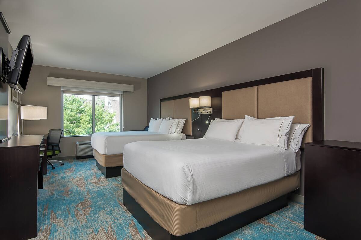 A hotel room with two beds, a desk, a TV, and a large window.