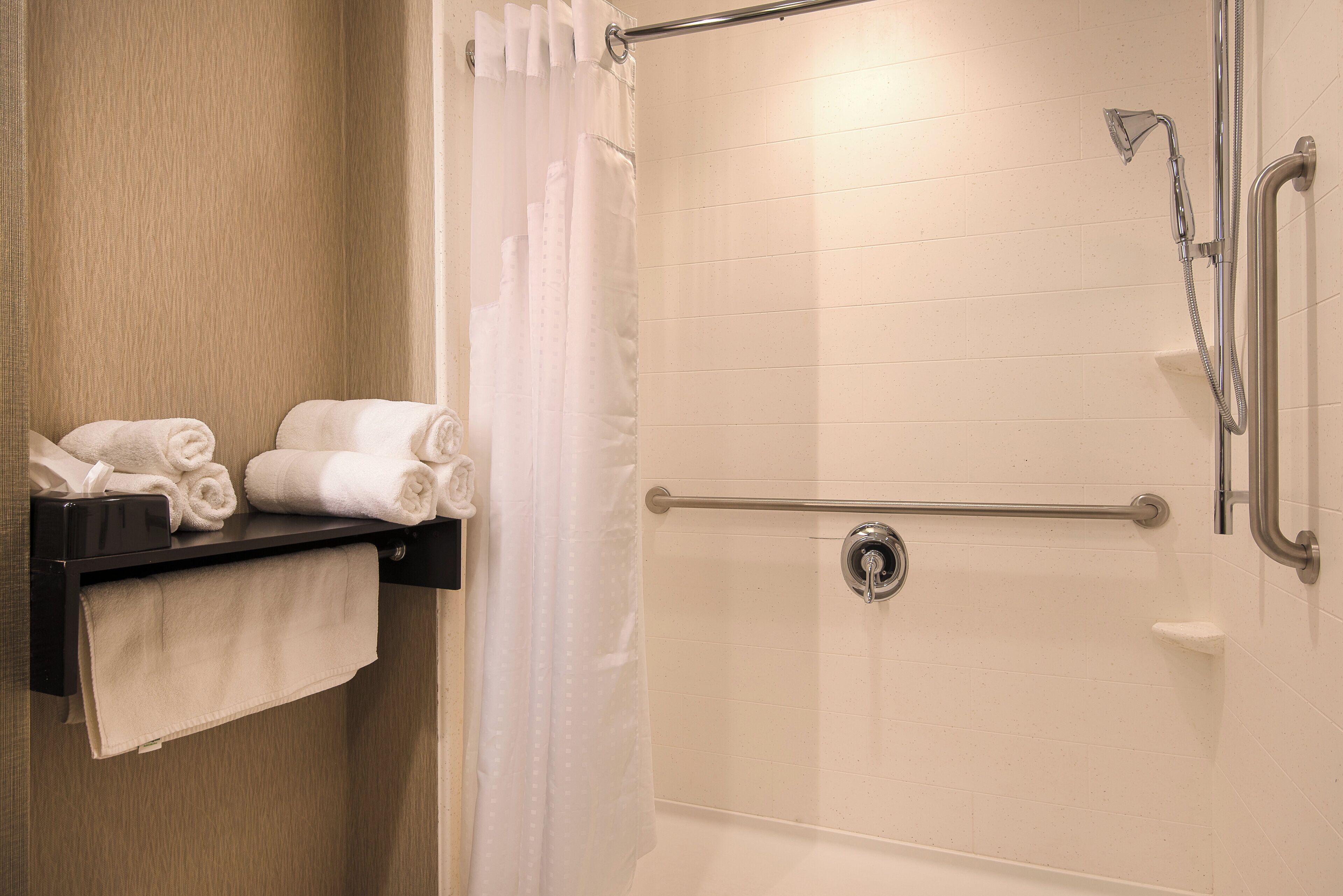A shower area with a grab bar, a towel rack with towels, and a shower curtain.