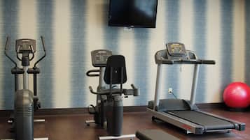 Une salle de sport équipée d’appareils de cardio, d’un téléviseur et d’un ballon d’exercice rouge.