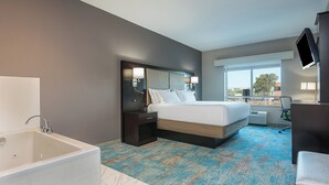 A hotel room with a large bed, a separate bathroom with a bathtub, a desk, and a TV mounted on the wall. - Holiday Inn Express & Suites Norwood-Boston Area by IHG (Norwood)