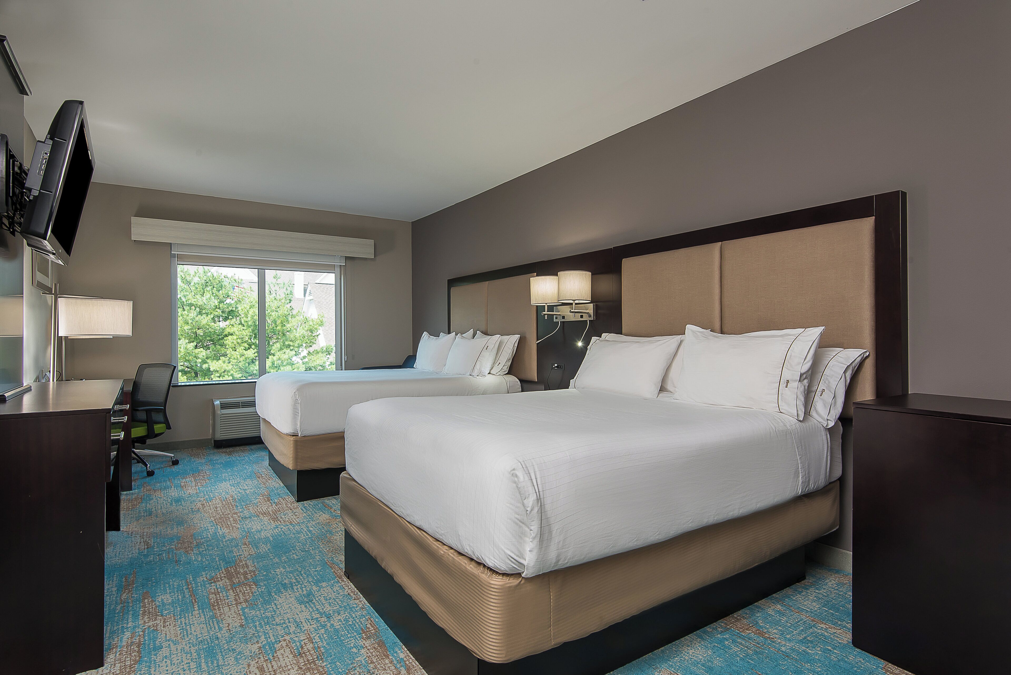 A hotel room with two beds, a desk, a TV, and a large window.