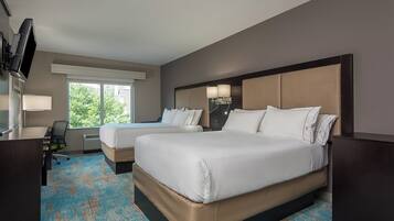 A hotel room with two beds, a desk, a TV, and a large window.