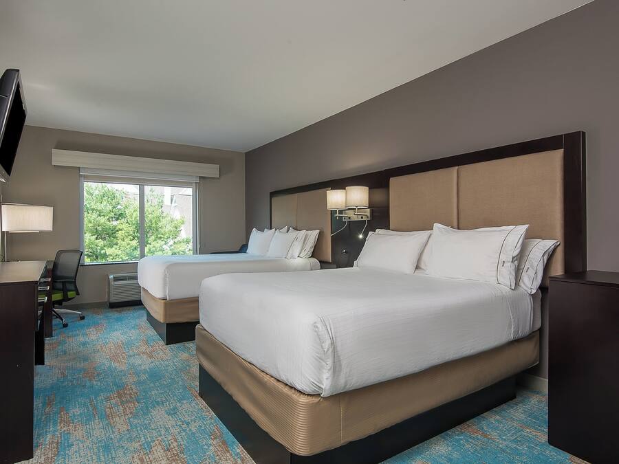 A hotel room with two beds, a desk, a TV, and a large window.