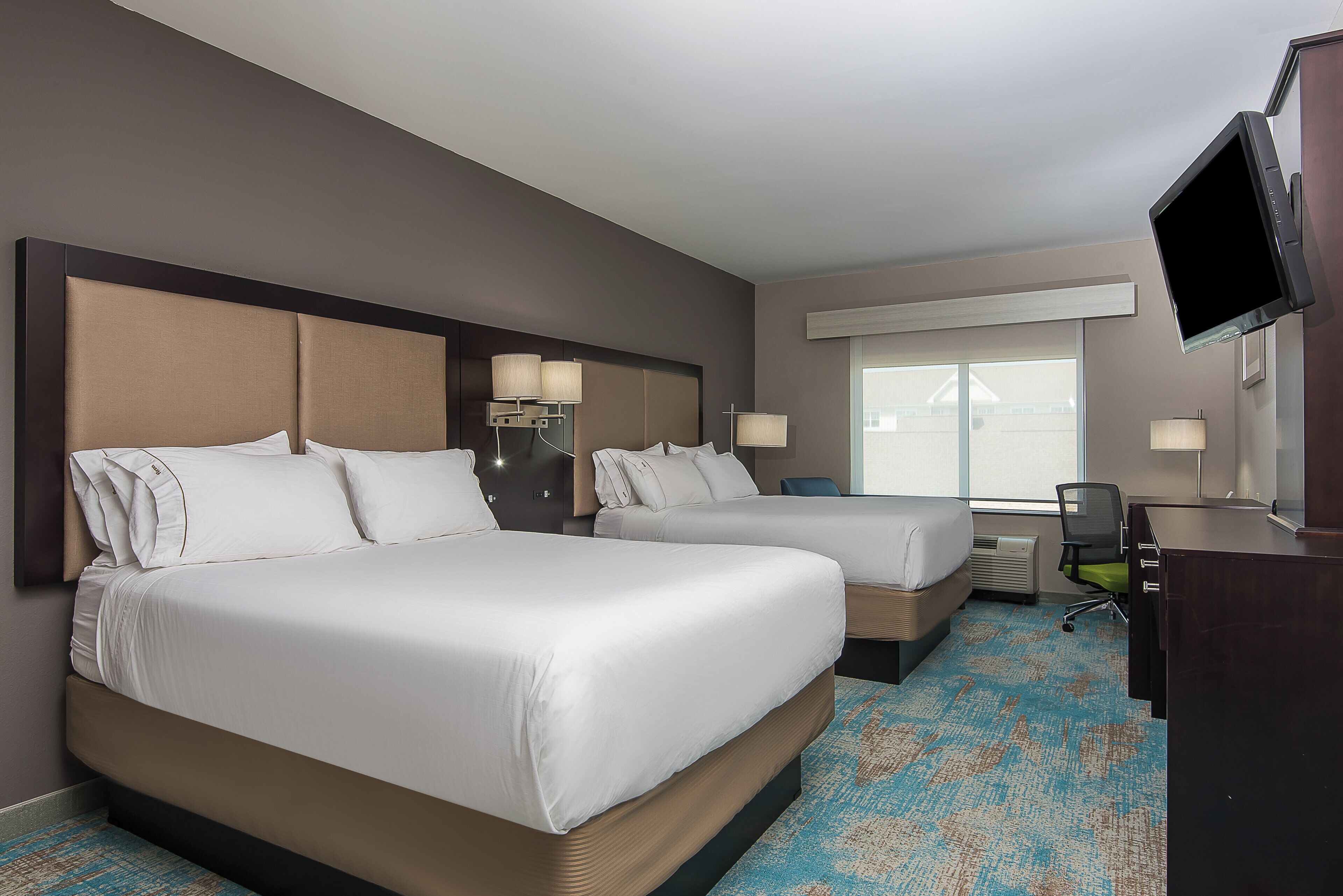Habitación de hotel con dos camas, un escritorio, una silla y un televisor.